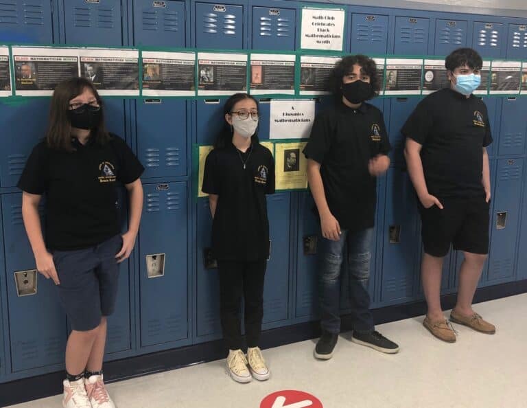 students wearing masks standin gin front of blue lockers wearing black shirts