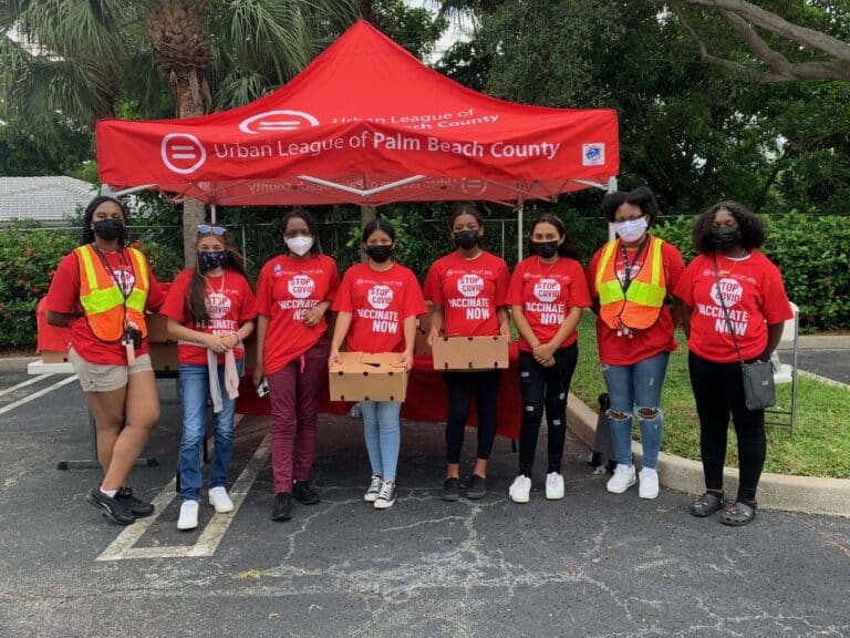 Group of volunteers wearing red holding boxes in front of a red tent