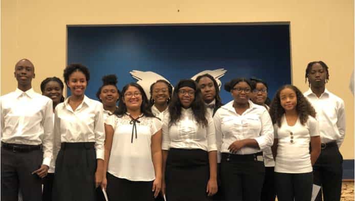 group of students smiling for a picture wearing white tops and black bottoms