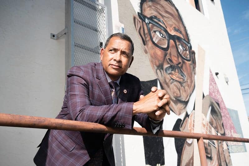 Man wearing a suit leaning over a railing with a mural of a man behind him