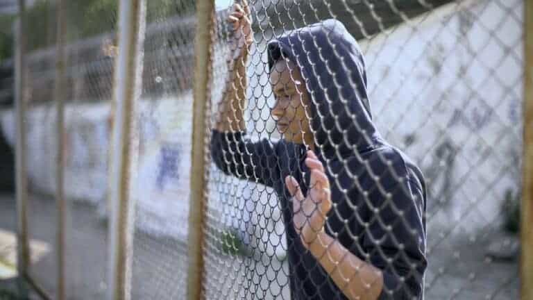 young man looking through chain link fence wearing dark colored hoodie