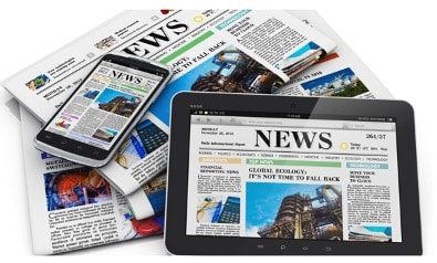 pile of newspapers, tablet and phone all showing news articles